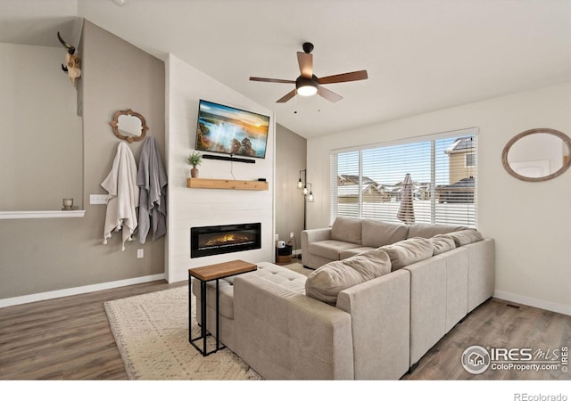 living room featuring lofted ceiling, wood-type flooring, a large fireplace, and ceiling fan