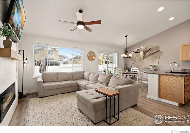 living room featuring ceiling fan with notable chandelier, a fireplace, lofted ceiling, sink, and light hardwood / wood-style floors