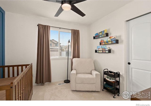 bedroom with light carpet, a crib, and ceiling fan