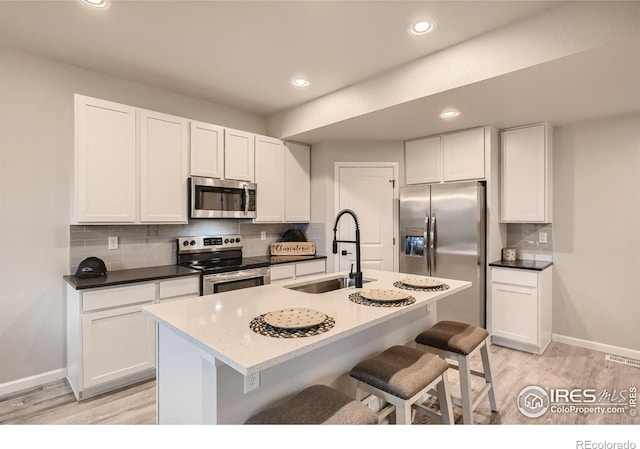 kitchen with a breakfast bar, a center island with sink, sink, appliances with stainless steel finishes, and white cabinetry