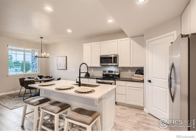 kitchen with a kitchen bar, stainless steel appliances, sink, decorative light fixtures, and a center island with sink