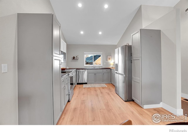 kitchen with gray cabinetry, stainless steel appliances, sink, light hardwood / wood-style flooring, and lofted ceiling