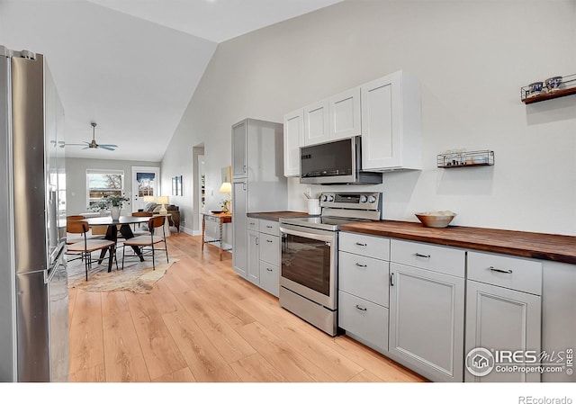 kitchen with ceiling fan, stainless steel appliances, high vaulted ceiling, wooden counters, and light wood-type flooring