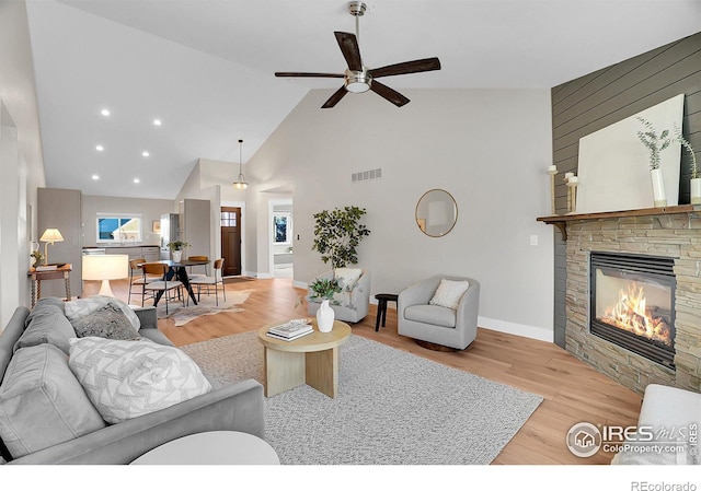 living room with ceiling fan, light hardwood / wood-style floors, a fireplace, and high vaulted ceiling