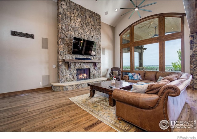 living room featuring ceiling fan, a fireplace, hardwood / wood-style floors, and a high ceiling