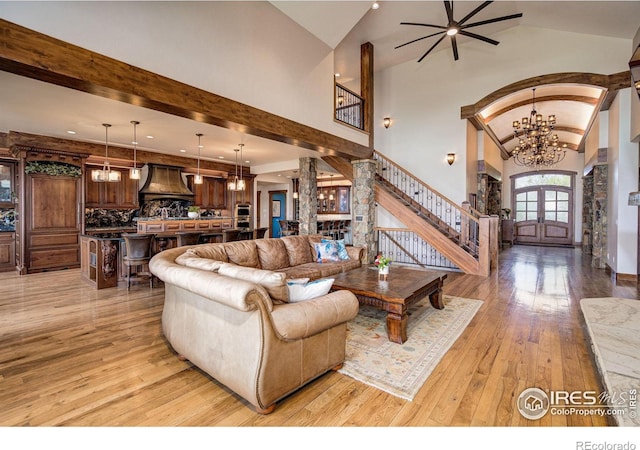 living room featuring decorative columns, light hardwood / wood-style flooring, high vaulted ceiling, and ceiling fan with notable chandelier