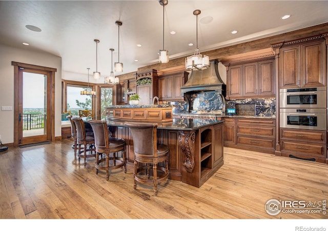 kitchen with a kitchen breakfast bar, backsplash, custom range hood, a spacious island, and pendant lighting