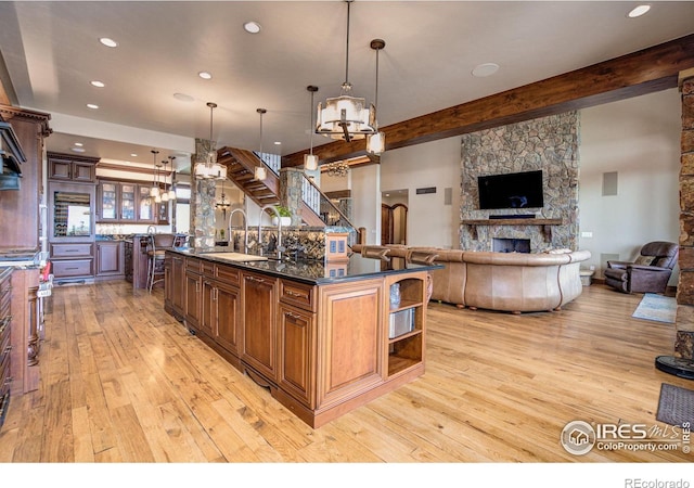 kitchen with sink, pendant lighting, beam ceiling, a stone fireplace, and a large island