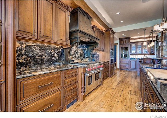 kitchen with tasteful backsplash, premium range hood, dark stone counters, pendant lighting, and double oven range