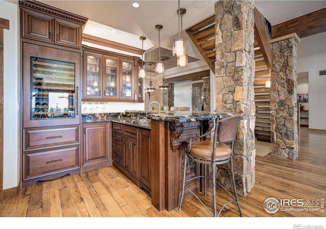 bar with sink, hanging light fixtures, dark stone countertops, light wood-type flooring, and beamed ceiling