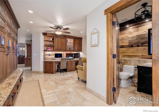 kitchen featuring ceiling fan, built in desk, and light stone counters