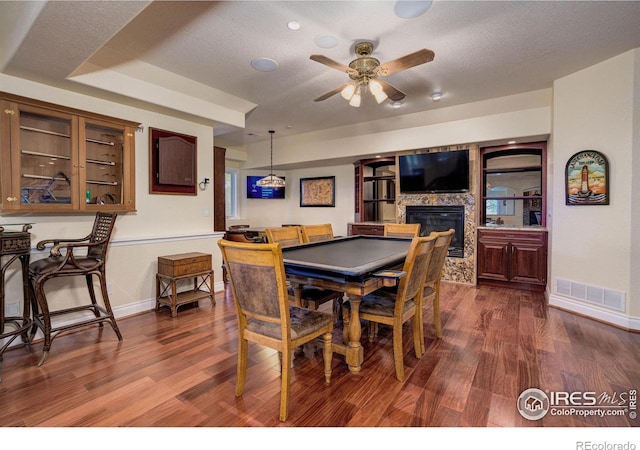 dining area with ceiling fan, a large fireplace, dark hardwood / wood-style flooring, a textured ceiling, and a tray ceiling