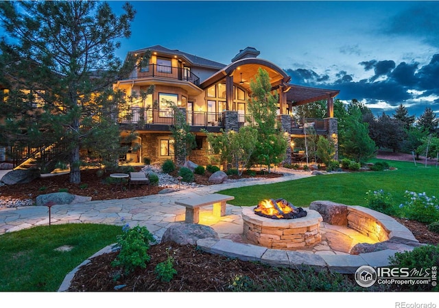 back house at dusk with a patio area, a balcony, a yard, and an outdoor fire pit