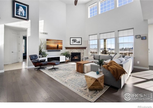 living room featuring a fireplace, wood-type flooring, a towering ceiling, and ceiling fan