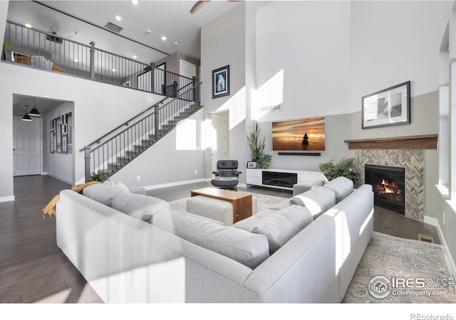 living room featuring a towering ceiling, dark wood-type flooring, and a tiled fireplace