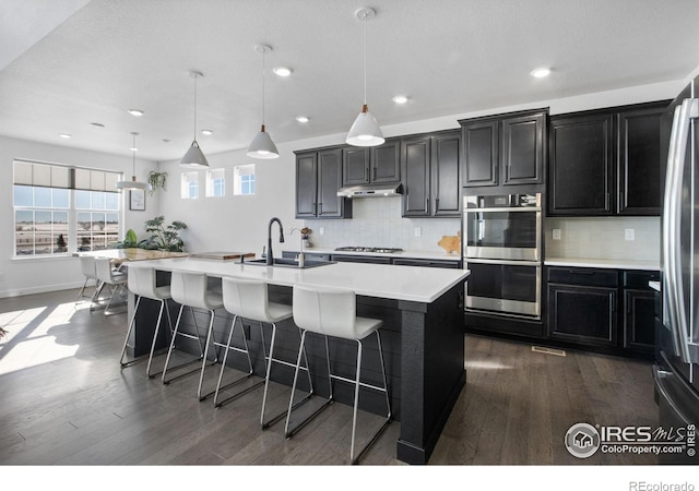 kitchen with a center island with sink, pendant lighting, sink, and appliances with stainless steel finishes