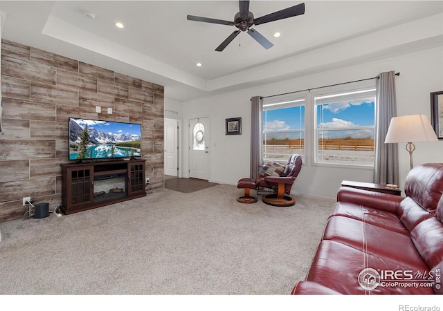 carpeted living room with a tray ceiling, recessed lighting, a ceiling fan, a glass covered fireplace, and baseboards