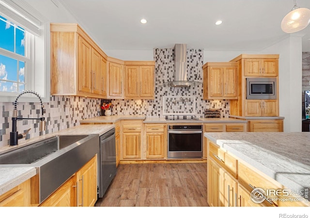 kitchen with light brown cabinets, stainless steel appliances, light countertops, wall chimney exhaust hood, and light wood finished floors