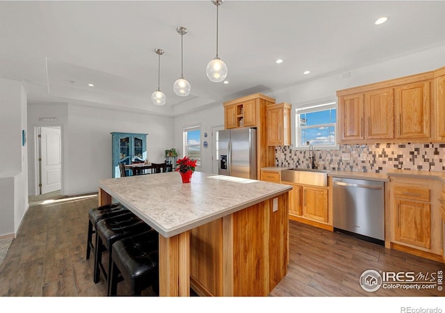 kitchen with stainless steel appliances, a kitchen island, a sink, backsplash, and dark wood finished floors