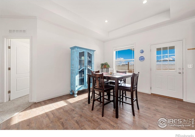 dining area with wood finished floors, a raised ceiling, visible vents, and recessed lighting