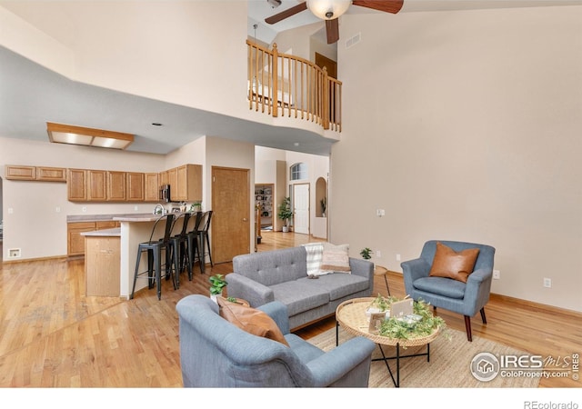 living room featuring light hardwood / wood-style flooring, a towering ceiling, and ceiling fan