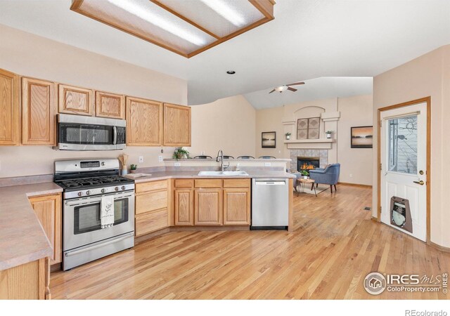 kitchen featuring light brown cabinets, appliances with stainless steel finishes, sink, a tiled fireplace, and light wood-type flooring