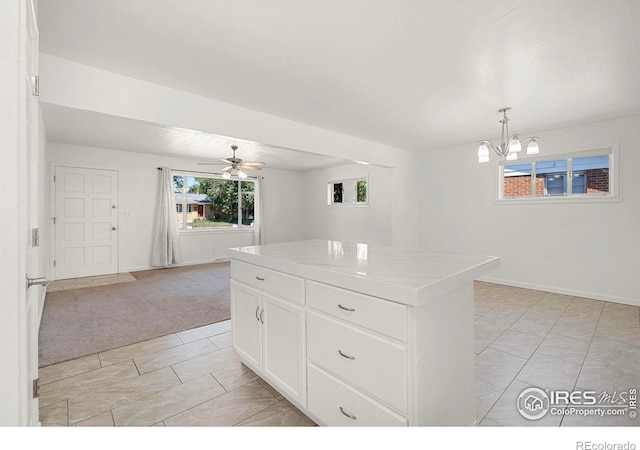 kitchen with a center island, decorative light fixtures, light carpet, white cabinets, and ceiling fan with notable chandelier