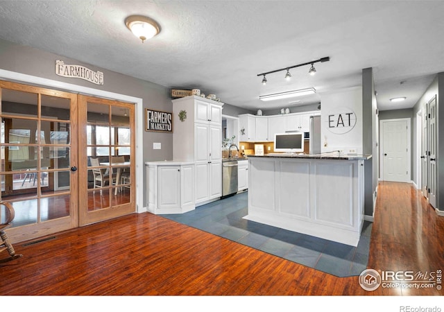 kitchen featuring dark tile patterned floors, stainless steel dishwasher, kitchen peninsula, a textured ceiling, and white cabinets