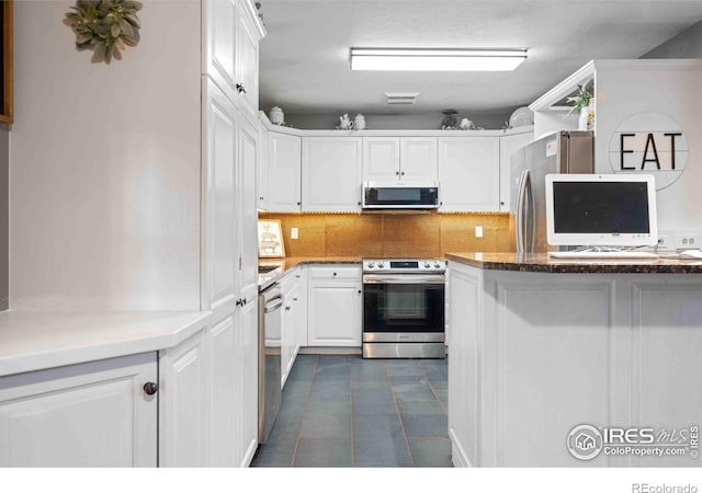 kitchen with appliances with stainless steel finishes, backsplash, dark tile patterned flooring, dark stone countertops, and white cabinetry