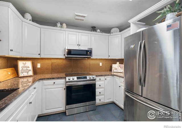 kitchen featuring white cabinets, backsplash, stainless steel appliances, and dark stone counters