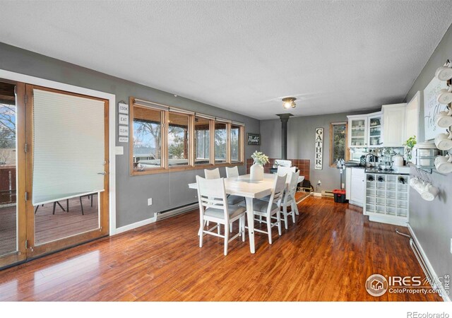 dining space featuring a wood stove, dark hardwood / wood-style flooring, a textured ceiling, and a baseboard heating unit