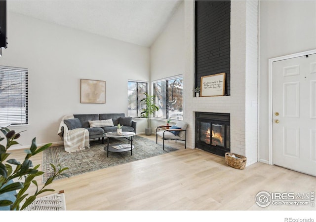 living room featuring high vaulted ceiling, a brick fireplace, and hardwood / wood-style flooring