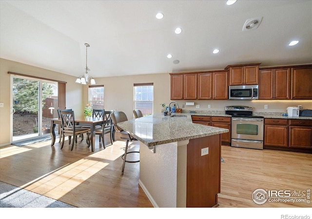 kitchen featuring kitchen peninsula, appliances with stainless steel finishes, a kitchen breakfast bar, a notable chandelier, and hanging light fixtures