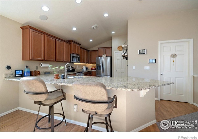 kitchen featuring a kitchen breakfast bar, light stone countertops, kitchen peninsula, and stainless steel appliances