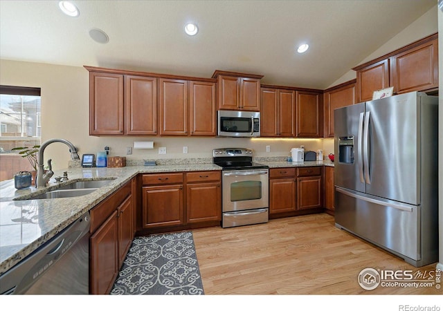 kitchen with lofted ceiling, sink, light stone countertops, appliances with stainless steel finishes, and light hardwood / wood-style floors