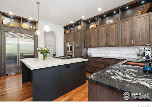 kitchen featuring dark brown cabinetry, a center island, hanging light fixtures, tasteful backsplash, and appliances with stainless steel finishes