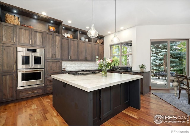 kitchen featuring appliances with stainless steel finishes, backsplash, a wealth of natural light, decorative light fixtures, and a center island