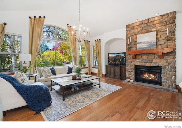 living room featuring an inviting chandelier, a stone fireplace, plenty of natural light, and hardwood / wood-style flooring