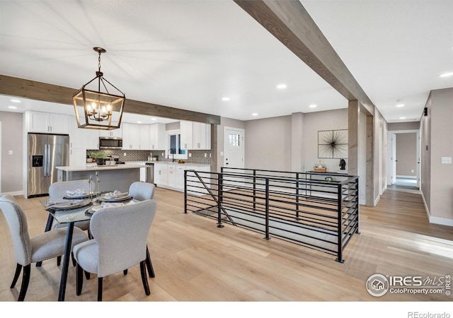 dining room with beam ceiling, sink, an inviting chandelier, and light hardwood / wood-style flooring