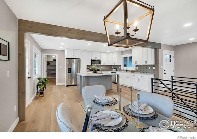 dining room with beamed ceiling, a notable chandelier, light hardwood / wood-style floors, and sink