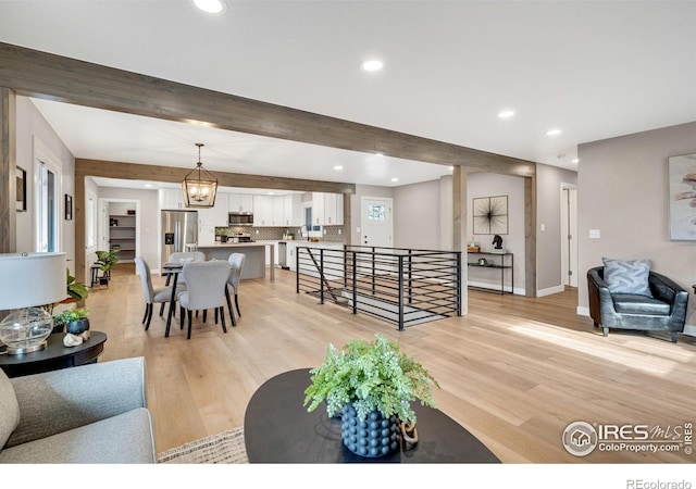 living room featuring beamed ceiling, light hardwood / wood-style floors, and an inviting chandelier