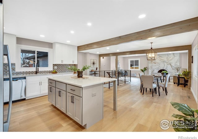 kitchen with stainless steel dishwasher, sink, pendant lighting, beamed ceiling, and a kitchen island