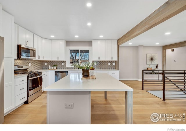 kitchen featuring white cabinets, a center island, stainless steel appliances, and beamed ceiling