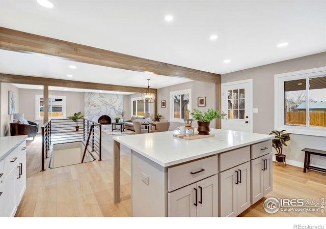 kitchen with beamed ceiling, light wood-type flooring, decorative light fixtures, and a kitchen island