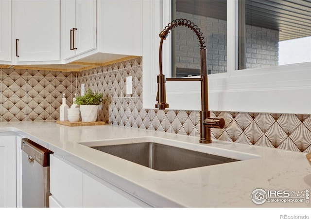 kitchen with sink, stainless steel dishwasher, decorative backsplash, light stone counters, and white cabinetry