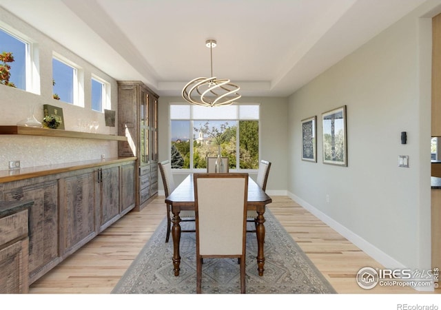 dining space with light hardwood / wood-style floors, a tray ceiling, and a notable chandelier