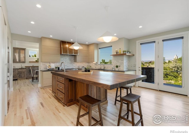 kitchen featuring sink, wooden counters, pendant lighting, a center island with sink, and light wood-type flooring