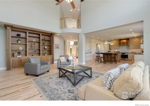 living room with a towering ceiling, light hardwood / wood-style floors, and ceiling fan