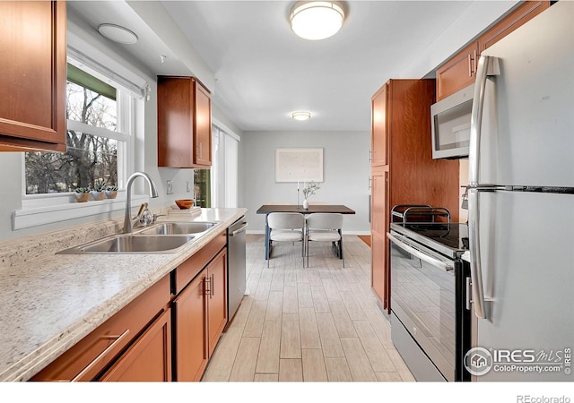 kitchen with light stone counters, sink, light wood-type flooring, and appliances with stainless steel finishes