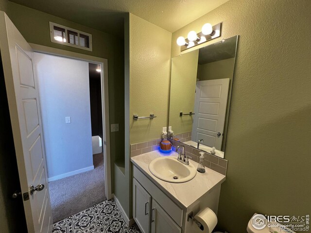 half bath with tasteful backsplash, visible vents, vanity, and baseboards